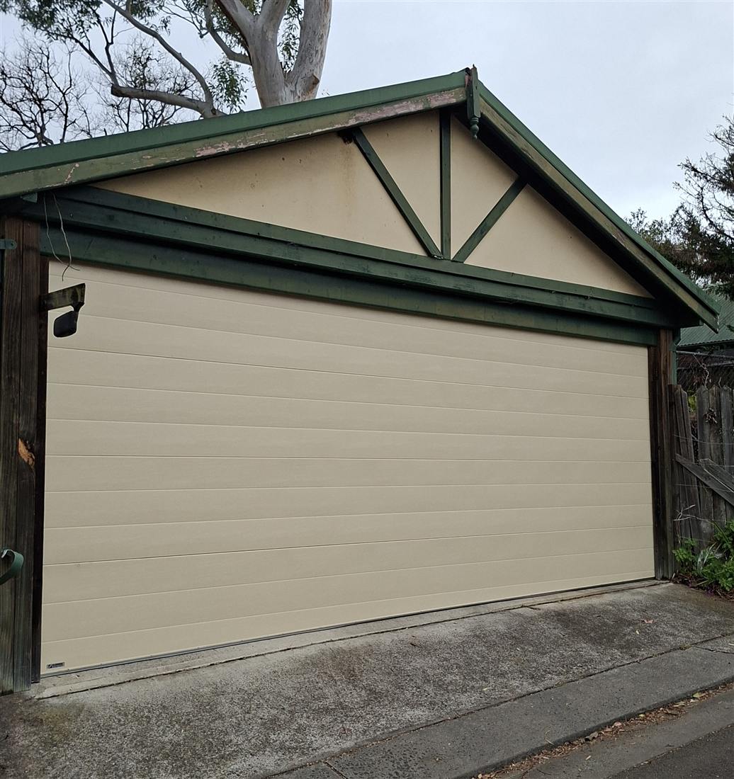 Cream garage door installation on a home with green trim
